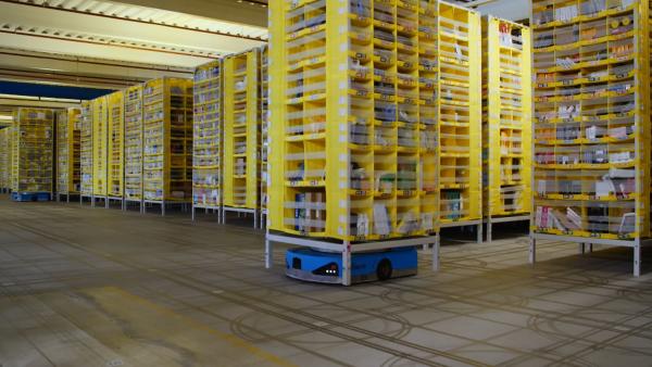 Bild 1 von 3: Blick in ein KI-unterstütztes Logistikzentrum von Amazon: Transportroboter bringen die Regale mit der benötigten Ware zu den Packern.