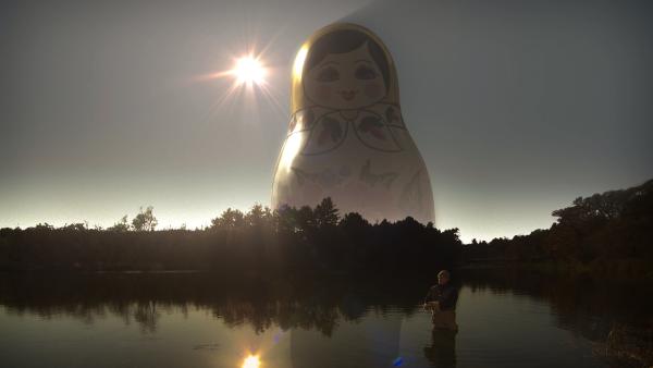 Bild 1 von 3: Russische Puppe erscheint über einem See - ein Zeichen der Mysterien des Universums.