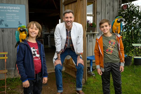 Bild 1 von 6: / Sam (Yann Cosack, li.), Liam (Nils Hofschneider, re.) und Papa Kajo (Jochen Schropp, mi.) vor der Tierarzt-Praxis mit zwei Papageien