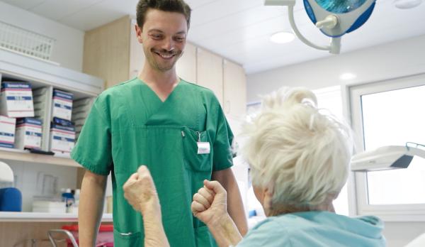 Bild 1 von 4: Ein Lächeln im Klinikalltag: Ein Pfleger und eine ältere Patientin teilen einen heiteren Moment.
