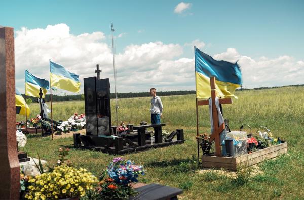 Bild 1 von 4: Der 15 Jahre alte Dennyk aus der Westukraine steht vor den Gräbern gefallener Dorfbewohner.