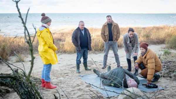 Bild 1 von 7: Das Team der SOKO Wismar um Revierchef Reuter (Udo Kroschwald 2.v.l.): Karoline Joost (Nike Fuhrmann 2.v.r.), Lars Pöhlmann (Dominic Boeer, M.) und Stine Bergendal (Sidsel Hindhede l.) versammeln sich um Dr. Helene Sturbeck (Katharina Blaschke). Diese kümmert sich bereits um die Leiche, Bucht-Ranger Richard Timpe (Peter Filthuth). Die Stimmung ist sehr betrübt, denn das Opfer ist ein Freund von Reuter. Wer hat den Wismarer Bucht-Ranger auf dem Gewissen?