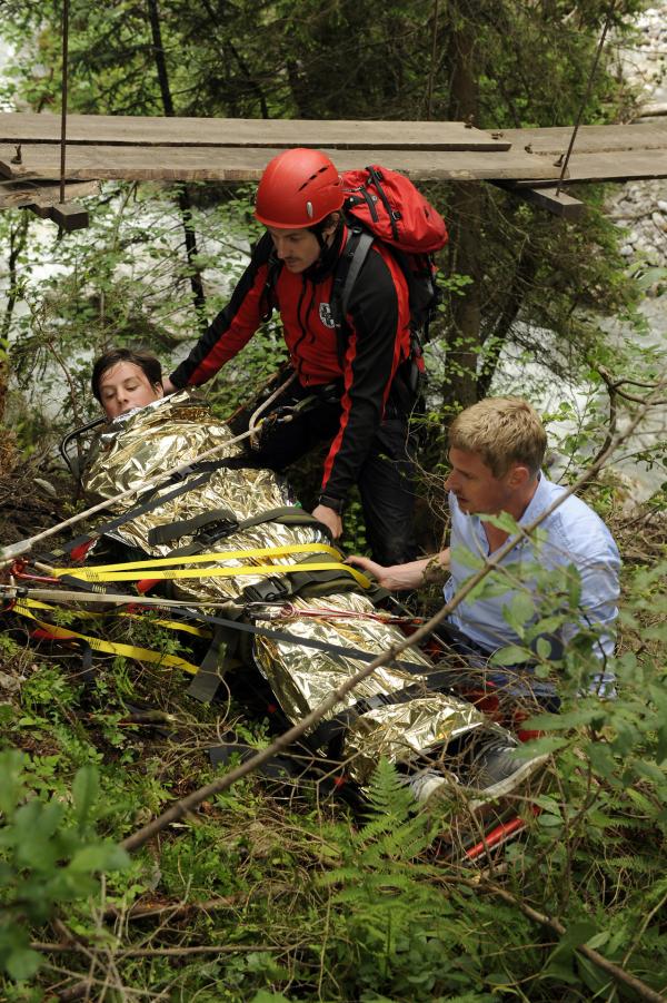 Bild 1 von 12: Andreas (Martin Gruber, r.) und Tobias (Markus Brandl, l.) bergen den unterkühlten und verletzten Max (Jonathan Beck, liegend) mit einer Rettungstrage.
