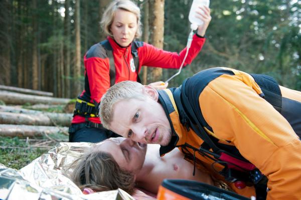 Bild 1 von 5: Während sich Jessika (Simone Hanselmann) um die medizinische Erstversorgung des verletzten Thomas (Alexander Becht, M.) kümmert, flüstert der Andreas Marthaler (Martin Gruber, r.) mit letzter Kraft zu, dass seine Freundin Sarah verschwunden ist.