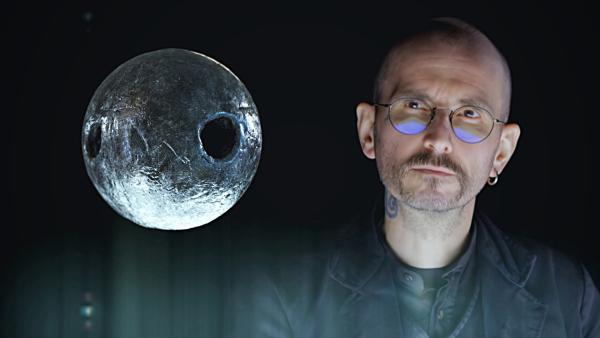 Bild 1 von 1: Der Kriminalbiologe Mark Benecke untersucht eine stecknadelkopfgroße, durchlöcherte Metallkugel, die im Körper eines toten Mannes gefunden wurde.