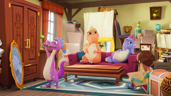 Bild 1 von 2: Die Dinos Socke, Trina und Doris leben sich in Oma Claras Kuriositätenladen ein. Socke  betrachtet sich in einem Spiegel, während Trina (2. von links) und Doris (3. von links) entspannt auf der Couch liegen. Leo sizt auf dem Boden und liest entspannt ein Buch über Dinosaurier.© KiKA/MACK Magic/Der Kinderkanal von ARD und ZDF, 2025- Honorarfreie Verwendung gemäß AGB im redaktionellen Zusammenhang mit genannter Sendung bei Nennung \