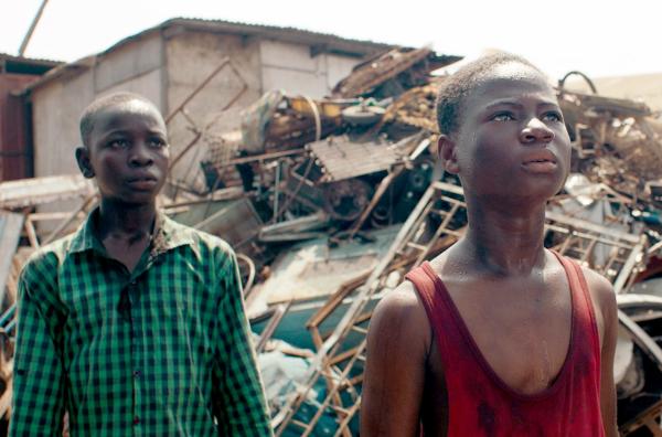 Bild 1 von 4: Kojo (Emmanuel Affedzi, re.) hat auf der Schrotthalde gearbeitet, statt zur Schule zu gehen, und wurde daraufhin von seinem Bruder Kofi (Jamal Baba, li.) zum Vater gebracht.