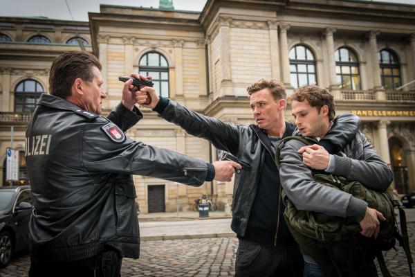 Bild 1 von 10: Lennard (Dominik Bliefert, M.) droht damit, Nick (Hauke Diekamp, r.) zu erschießen, falls Hans (Bruno F. Apitz, l.) näher kommt. Doch Hans geht aufs Ganze.