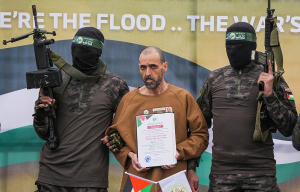 Bild 1 von 1: Der israelische Geiselnehmer Eli Sharabi, der seit dem 7. Oktober 2023 von der Hamas im Gazastreifen als Geisel festgehalten wurde, steht am 8. Februar 2025 auf einer Bühne in Deir al-Balah im zentralen Gazastreifen, begleitet von Hamas-Kämpfern, bevor er dem Roten Kreuz übergeben wird. (AP Photo/Abdel Kareem Hana, Archivaufnahme)