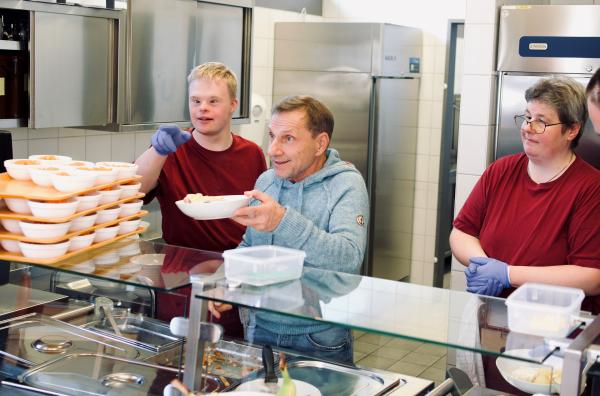 Bild 1 von 4: Richy Müller (M.) unterstützt das Team der Hauswirtschaft des BHZ Stuttgart bei der Essensausgabe.