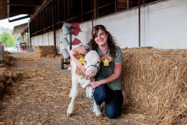 Bild 1 von 8: Veronika Kirchmaier sitzt im Stall und hält ein Kalb in den Armen.