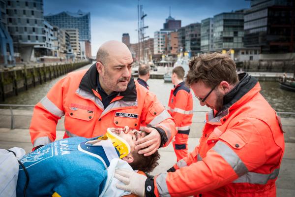Bild 1 von 9: Dr. Aguilar (Gabriel Munoz Munoz, l.) und sein Kollege (Komparse) kümmern sich um Viktor (Patrick Mölleken, M.), der vor seinem Ruderclub brutal zusammengeschlagen wurde.