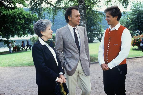 Bild 1 von 1: Prof. Brinkmann (Klausjürgen Wussow, M.) und Käti (Karin Hardt, l.) haben ein Wiedersehen mit Mischa (Jochen Schroeder, r.), der zu ihrem Erstaunen beim Kurkonzert Trompete bläst.