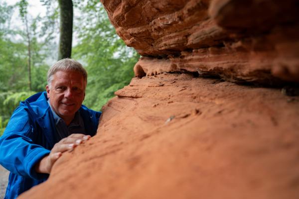 Bild 1 von 7: Colin Devey betrachtet den roten Sandstein, der in der Pfalz allgegenwärtig ist. Er ist der solide Untergrund auf dem der Pfälzerwald ruht. Das Gestein ist vor 250 Millionen Jahren entstanden, als urzeitliche Flüsse in einer sonst trockenen Wüstenlandschaft ihre Sedimente ablagerten. Eisenoxide verleihen dem Buntsandstein seine rötliche Färbung.