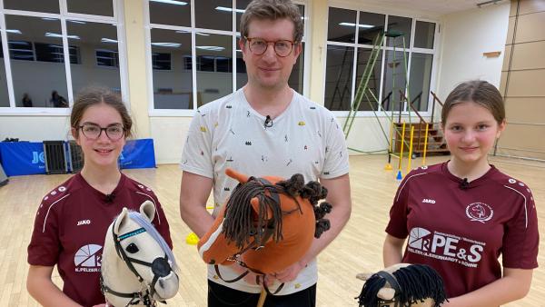 Bild 1 von 1: Melina und Rebecca sind begeisterte Hobby Horse-Reiterinnen und zeigen Robert, worauf es bei der Trendsportart ankommt.