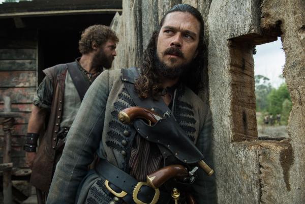 Bild 1 von 11: John Silver (Luke Arnold) hat Billy, den ehemaligen Sklaven auf der Underhill-Plantage, ausgeliefert, um das Bündnis mit den Sklaven wieder zu erneuern. Was er allerdings nicht weiß: Zur gleichen Zeit haben die Spanier begonnen, Nassau vollkommen zu zerstören ...