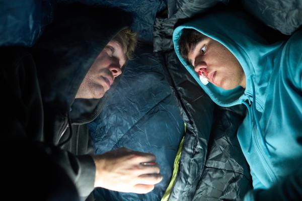 Bild 1 von 6: Provisorisch in Schlafsäcke gewickelt liegen Julian (Ben Münchow, l.) und Ernst (Diyar Ilhan, r.) vor der Notaufnahme, wo Ernsts gebrochene Nase behandelt werden soll. Die hat er einem versehentlichen Fausthieb des Schuldirektors Stöfgen zu verdanken.