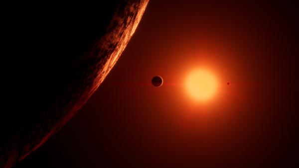 Bild 1 von 8: Trappist 1 ist ein Roter Zwerg. Er hat nur 10 Prozent der Masse der Sonne und 1 Prozent ihrer Helligkeit. Sein rotes Licht erhellt schwach seine sieben erdgroßen Planeten.