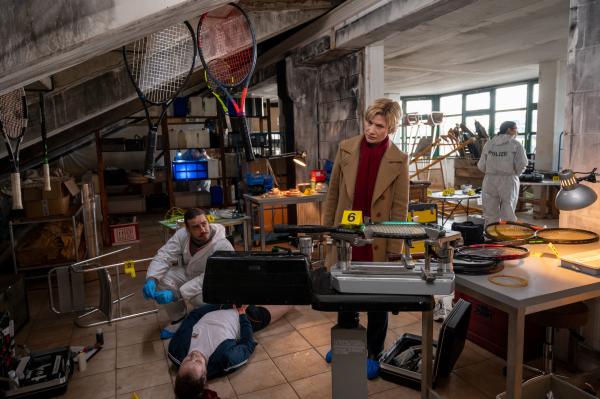 Bild 1 von 3: Am Tatort: Hier wurde Tennistrainer Timo Heinrichs (Komparse) ermordet, nachdem er im Geräteschuppen des Vereins an einen Stuhl gefesselt wurde. Kriminalhauptkommissarin Martina Seiffert (Astrid M. Fünderich) ist bereits am Ort des Verbrechens, wo sie mit dem Rechtsmediziner Dr. Benedikt Förster (Florian Wünsche) ersten Spuren nachgeht.