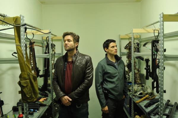 Bild 1 von 6: Rico Sander (Benjamin Strecker, r.) hat eine interessante Entdeckung gemacht: In der Waffenkammer des Bunkers zeigt er Jo Stoll (Peter Ketnath, l.) das Waffenarsenal des Prepper-Vereins. Darunter auch Armbrüste.