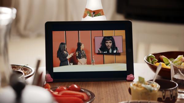 Bild 1 von 5: Auf einem Tablet ist die Kultursendung zu sehen, in die Jo (Salka Weber) eingeladen worden ist. Von links: Moderation: Samira El Quassil, Expertin: Ciani-Sophia Höder und Jo (Salka Weber).