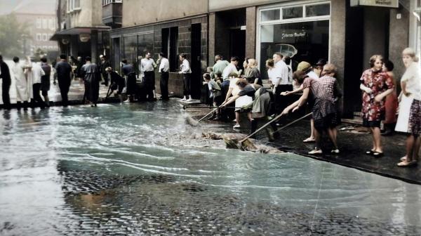 Bild 1 von 5: Die Geschäftsleute in der Giersstr. versuchen mit vereinten Kräften das Wasser aus den Läden herauszuhalten.(Foto nachcoloriert mit KI)
