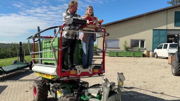 Bild 1 von 5: Im Bild: Obstbauer Wolfgang und Lena fahren auf einem Erntefahrzeug zur Apfelplantage.