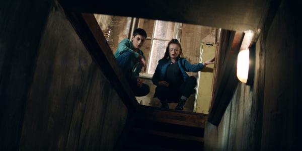 Bild 1 von 5: Bea (Aoife Hughes, r.) und Louis (Oliver Cunliffe) sind in der Hütte eingeschlafen. Am Morgen entdecken sie Stromkabel, die möglicherweise für die Licht- und Geräuscheffekte in der Nacht gesorgt haben, und eine Falltür zu einem Keller.
