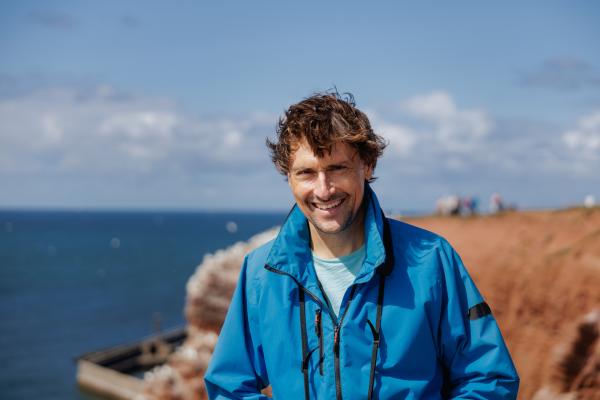 Bild 1 von 5: Uli Kunz steht lächelnd auf dem Lummenfelsen. Im Hintergrund nisten die Basstölpel.