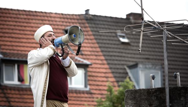 Bild 1 von 3: Nuri Hodscha (Hilmi Sözer) greift zu drastischen Mitteln: er gibt den Muezzin und ruft von den Dächern von Lautringen zum Gebet.