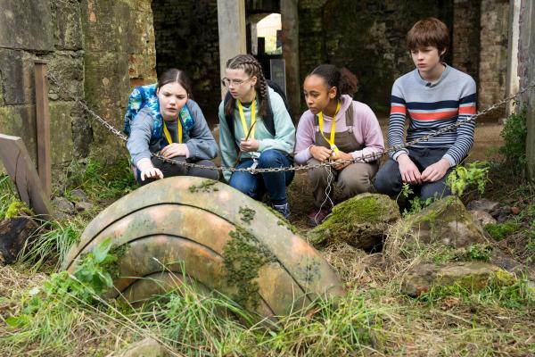 Bild 1 von 3: Im Rückblick entdeckt die damals noch vollständige Control-Alt-Gruppe - Isabel (Alis Waters, l.), Monika (Lucy Chambers, 2.v.l.), Faye (Keira Chansa, 2.v.r.) und Luka (Pádraig McCormack, r.) - das Artefakt in einem kleinen Burggarten in einer Ruine. Damals auf einer Klassenfahrt hatten sie den ersten Kontakt mit ihrem Artefakt.