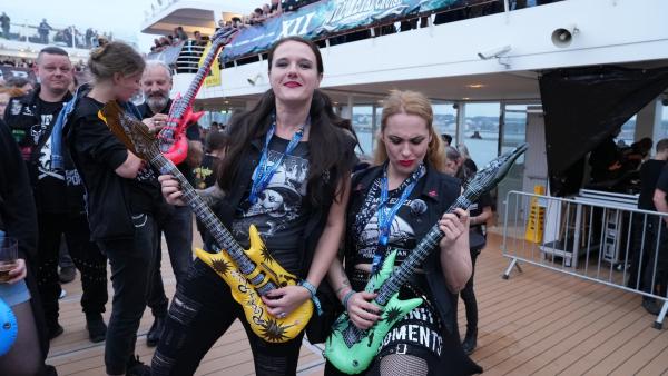 Bild 1 von 1: Heavy Metal-Fans Vanessa Wüpping (l.) und Birte McNeely (r.) posieren mit aufblasbaren Gitarren an Deck.