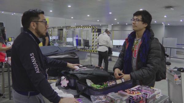 Bild 1 von 3: Ein Zollbeamter befragt einen Reisenden aus den USA, dessen Koffer voller Sammlerfiguren für Misstrauen sorgt.