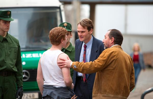 Bild 1 von 4: Peter Simon (Fabian Hinrichs, M.) versucht Reiko Böttcher (Leon Seidel, l.) zu konfrontieren. Hajo Gärster (Thorsten Merten, r.) kommt seinem Neffen jedoch zu Hilfe. (mit Komparsen im HG.).