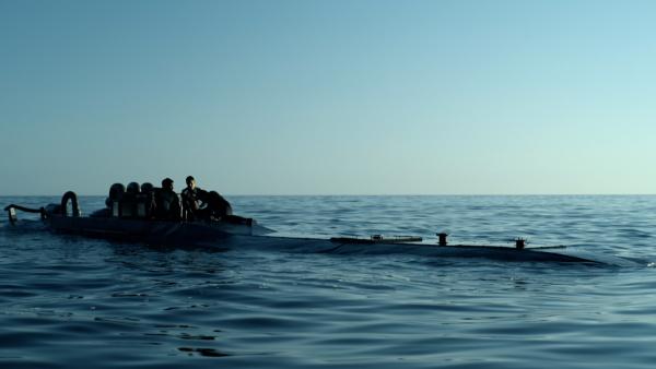 Bild 1 von 5: Nando (Álex González, M.), Angelito (David Trejos, r.) und Walder (Leandro Firmino, l.) beraten sich darüber, wie sie die Ware an der Küste entladen können, ohne dabei von der Polizei erwischt zu werden.