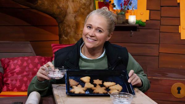 Bild 1 von 1: Singa hat Kekse gebacken und möchte sie verzieren. Nachdem sie ins Fernrohr geschaut hat, sind diese schon voller bunter Streusel. Da können  nur die Wichtel dahinterstecken!