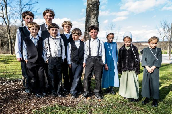 Bild 1 von 1: Im Bild: Eine Gruppe von Amish-Kindern stehen vor einem Baum.