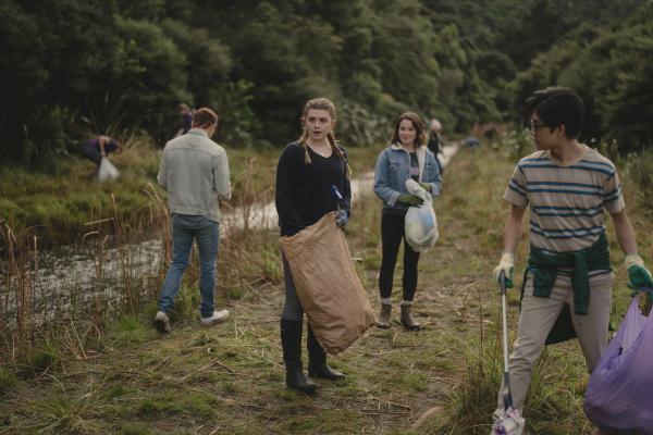 Bild 1 von 4: Issie (Macey Chipping, 2.v.r.), Natascha (Antonia Robinson, 2.v.l.) und Caleb (Joshua Tan, r.) helfen den Bewohnern von Kauri Point bei der Müllsammelaktion. Es ist erschreckend, wie viel Müll die Touristen in der Wildnis hinterlassen haben.