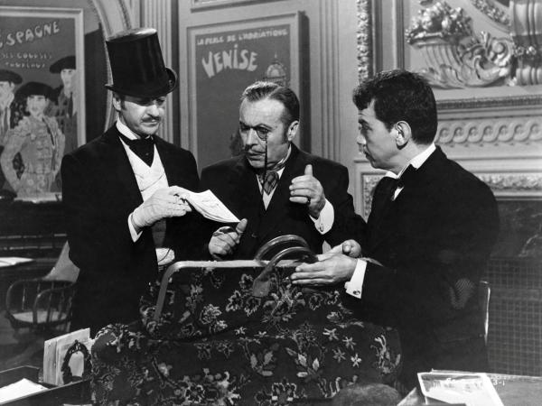 Bild 1 von 11: Medium shot of David Niven as Phileas Fogg looking through papers in briefcase while Robert Newton as Mr. Fix and Cantinflas as Passepartout watch.