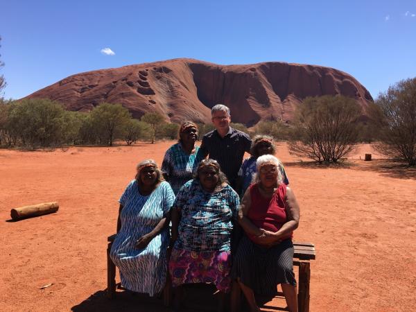 Bild 1 von 4: Sir Christopher Clark vor dem heiligen Berg Uluru - mit Frauen des Stammes der Anangu.