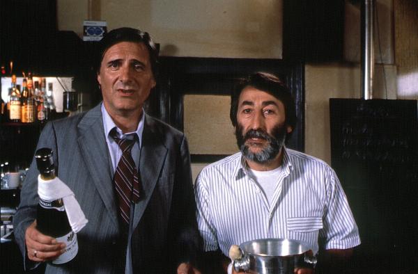 Bild 1 von 3: Josef Haslbeck (Helmut Fischer, links) preist sich mit Erfolg Giancarlo (Aurelio Ferrara) an - nur so kann er wieder einmal dem drohenden Rausschmiß von Ilse entgehen.