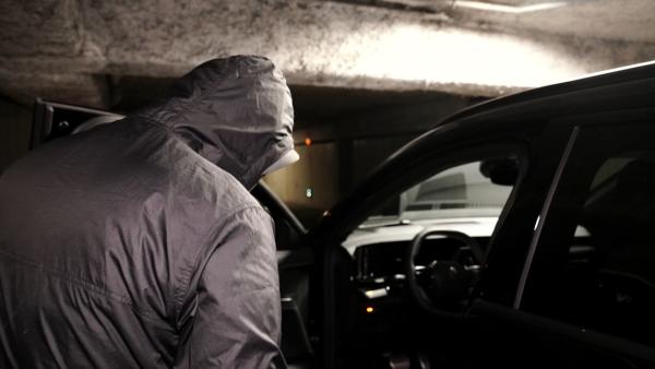 Bild 1 von 1: Ein vermummter Mann öffnet die Fahrertür eines Autos in einer Tiefgarage.
