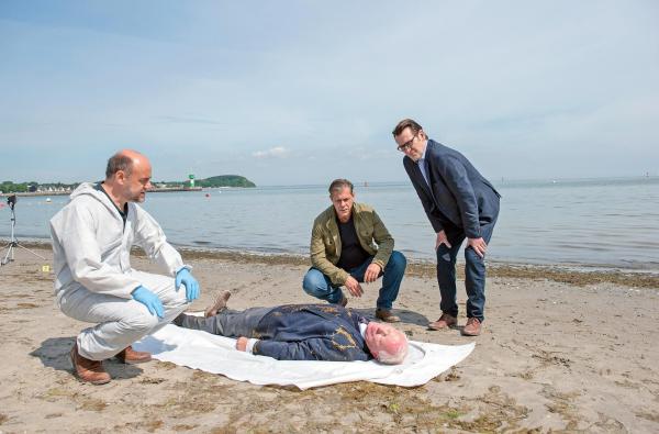 Bild 1 von 3: Im Bild: Die Leiche von Frank Loose (Arne Fuhrmann, liegend.) gibt den Kommissaren Finn Kiesewetter (Sven Martinek, 2.v.r.) und Lars Englen (Ingo Naujoks, r.) und Rechtsmediziner Dr. Henning Strahl (Christoph Tomanek, l.) einige Fragen auf.