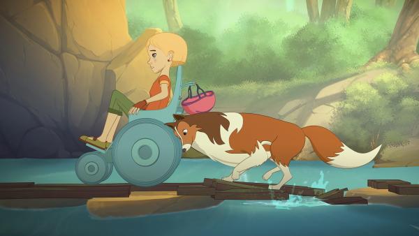 Bild 1 von 3: Lassies hilft Judith, über die behelfsmäßige Brücke auf die andere Flussseite zu kommen, wo die Wanderung fortgesetzt werden soll.