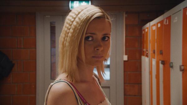 Bild 1 von 2: Selina (Elli Rhiannon Müller Osborne) kommt an ihrem Spind in der Schule an. Auf dem Spind liest sie eine fiese Nachricht, die von ihren Mitschülern geschrieben ist.