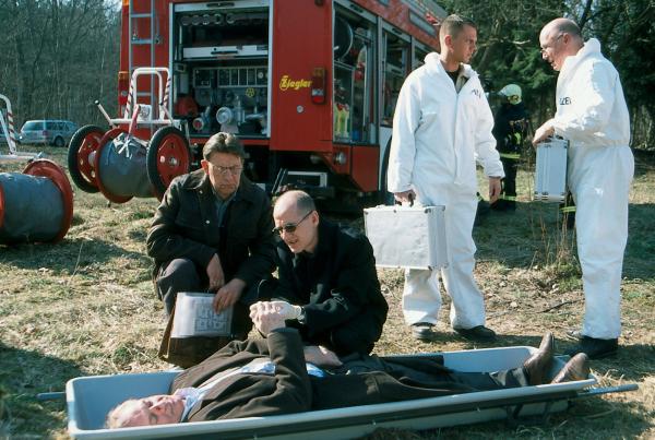 Bild 1 von 10: Dr. Robert Kolmaar (Ulrich Mühe, r.) und Kommissar Joe Hoffer (Jörg Gudzuhn, l.) werden zu dem Unfallort von David Taylor (Matthew Burton) gerufen.
