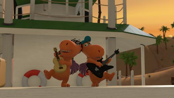 Bild 1 von 2: Auf dem Deck eines Schiffes stehen Kokosnuss und der Rockstar Rocko Rolla. Beide spielen Gitarre und sind nicht auseinander zu halten.