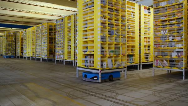 Bild 1 von 2: Blick in ein KI-unterstütztes Logistikzentrum von Amazon: Transportroboter bringen die Regale mit der benötigten Ware zu den Packern.