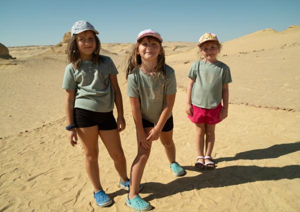 Bild 1 von 6: Die drei Mädchen Maja, Lilly und Mia stehen in der Wüste vor hohen Sanddünen.
