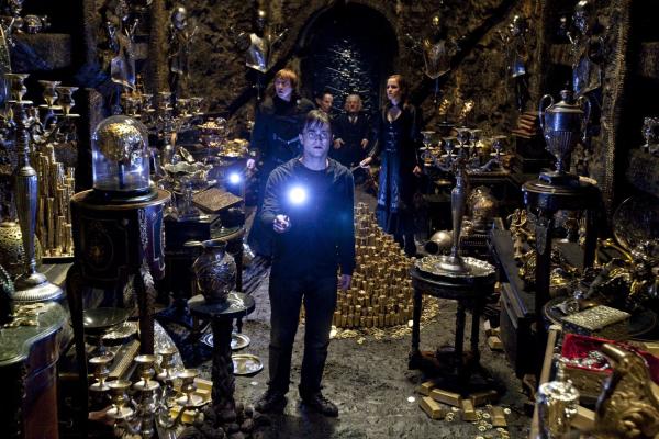 Bild 1 von 7: Daniel Radcliffe as Harry Potter, holding glowing wand in foreground, and Rupert Grint as Ron Weasley, Warwick Davis as Griphook, Gringotts goblin, and Emma Watson as Hermione Granger, in background, all inside Bellatrix's vault